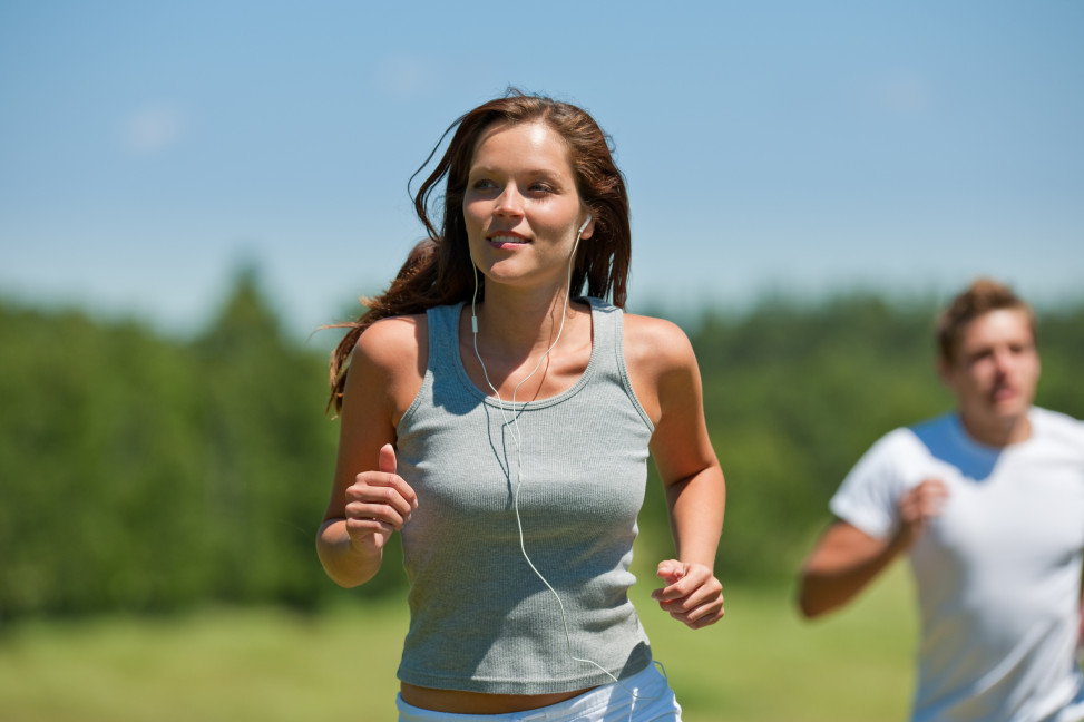Brown hair woman with headphones jogging, man in background, shallow DOF
